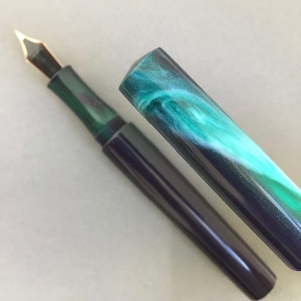 Close-up of fountain pen cap which has the shape of a swirling green shape in it